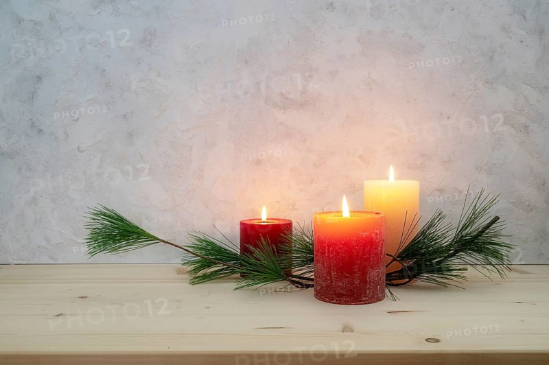 Three candles lit for the third Advent, pine branch as a simple, minimal decoration on a light wooden board against a rustic plaster wall, large copy space, selected focus