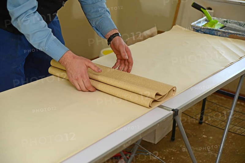 A man rolls up some glued wallpaper, ready to decorate a bedroom