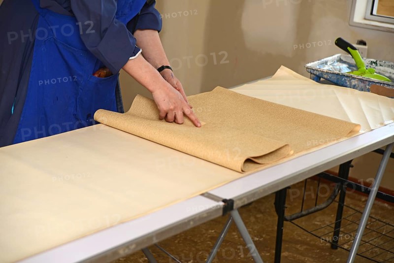 A woman rolls up some glued wallpaper, ready to decorate a bedroom