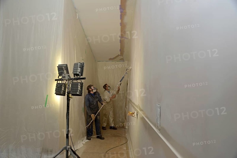 Two tradesman use airless spray equipment to paint a top coat on the walls of a commercial building