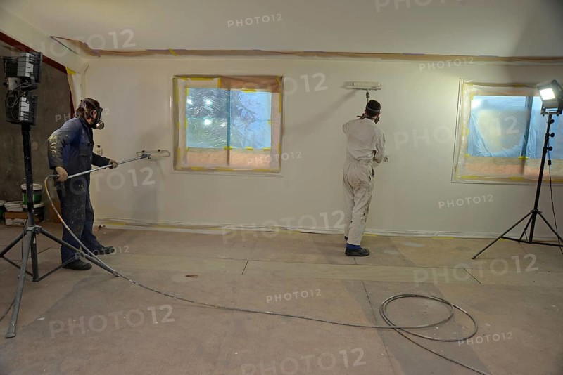 A tradesman using airless spray equipment to paint a top coat on the walls of a commercial building