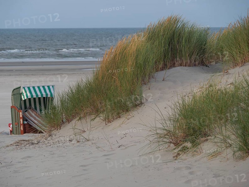 A wind-protected beach chair stands between dunes and grasses on the beach with a view of the sea and the cloudy sky, juist, east frisia, Germany, Europe