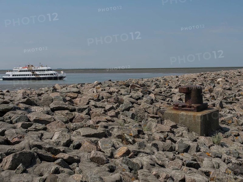 A ferry sails along a rocky coast under a clear sky, the scene looks industrial and natural at the same time, Hallig Hooge, schleswig-holstein, germany