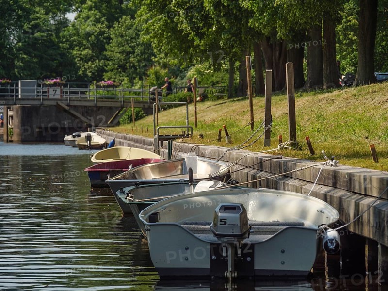 Boats along a canal, moored to wooden piles, shore with trees under a summer sky, friedrichstadt, schleswig-holstein, germany