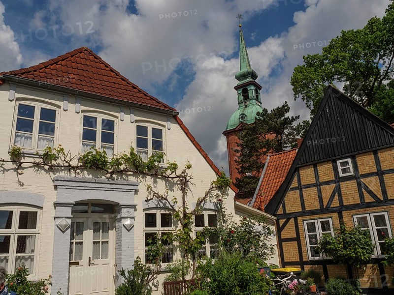 A historic street with half-timbered houses, flowers and a church tower under a cloudy sky with sun, Kappeln, Schleswig-Holstein, Germany, Europe