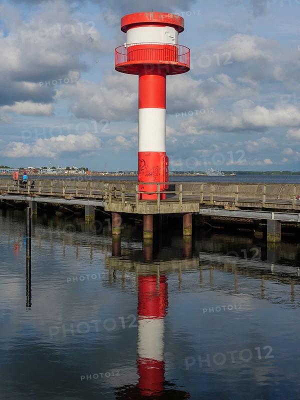 Lighthouse in red and white at the pier, reflecting on calm water under partly cloudy sky, Eckernförde, Schleswig-Holstein, Germany, Europe