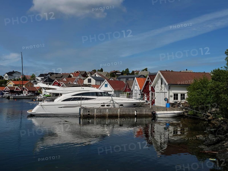 White yachts in the harbour in front of houses with red roofs. Calm water reflects the boats and houses, Stavanger, Norway, Europe