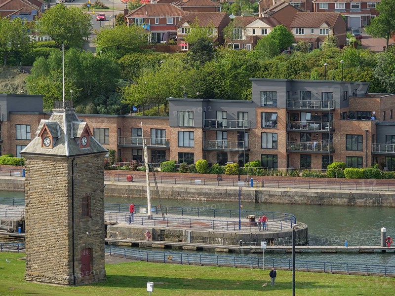 Stone tower on the riverside with modern residential buildings in the background, people walking on the lawn, tynemouth, England, Great Britain