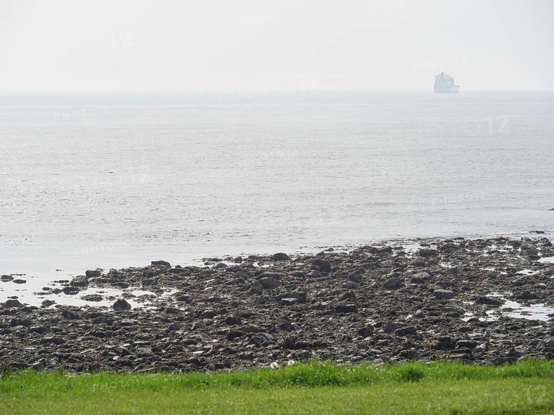 View of a rocky coastline merging into the open sea, a ship can be seen on the horizon in the fog, Newcastle, England, Great Britain