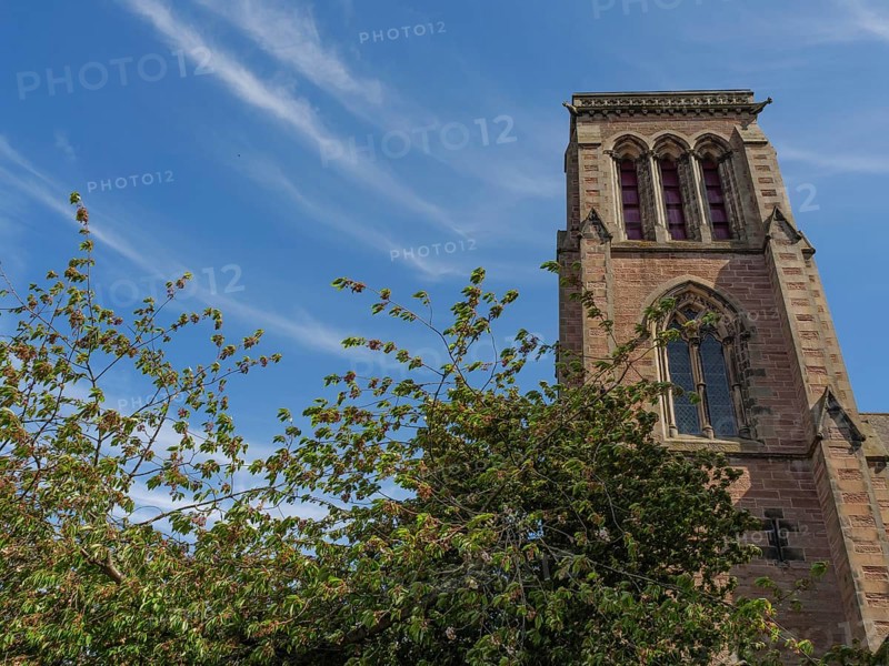 The gothic tower of a church in front of a sky with clouds and surrounded by trees, inverness, Scotland, Great Britain
