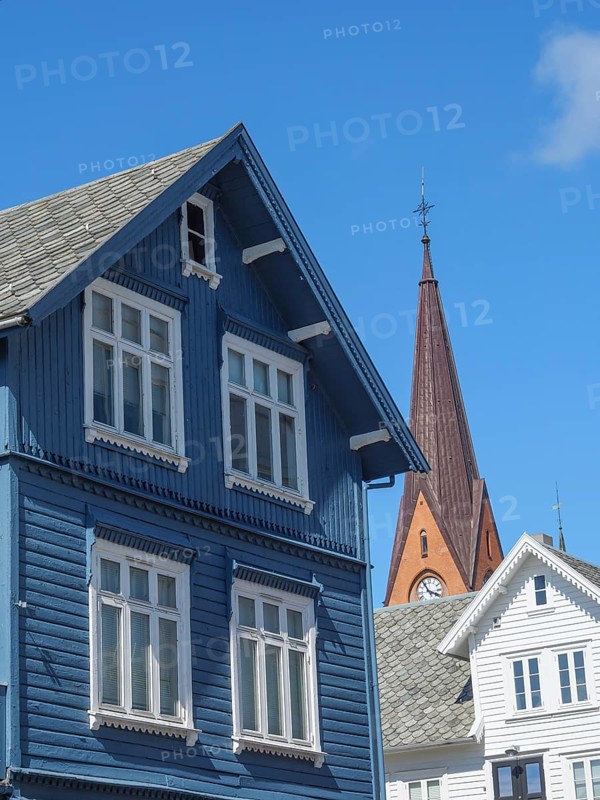 Blue wooden house with white windows in front of a red church tower under a bright blue sky, Haugesund, Norway, Europe
