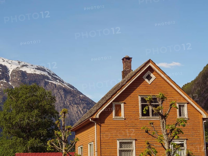 A brown wooden house with a high roof in front of a mountain panorama under a clear sky, Eidfjord NOR 3