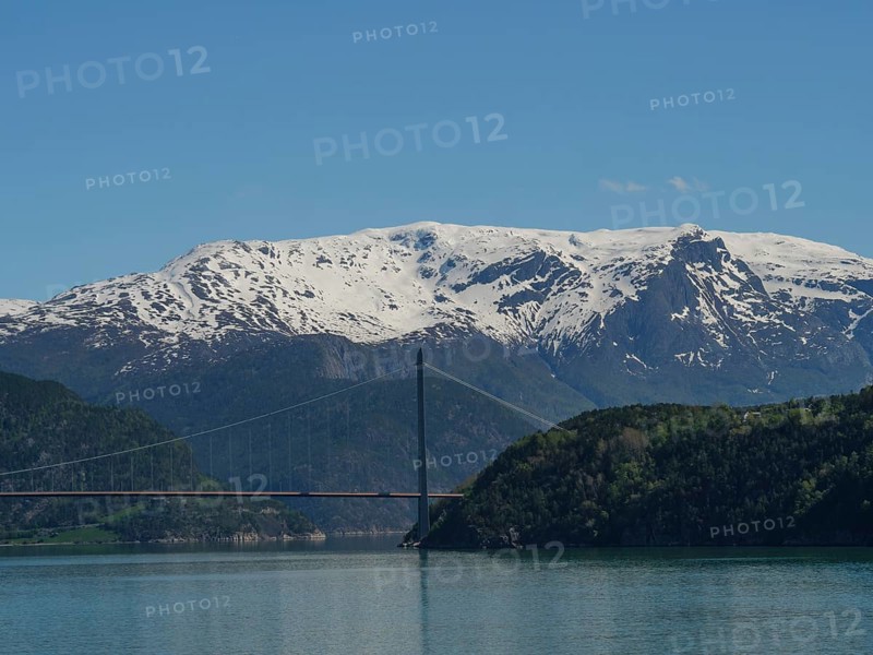 Suspension bridge over a fjord with snow-capped mountains in the background, blue sky and calm atmosphere, Eidfjörd, Norway, Europe