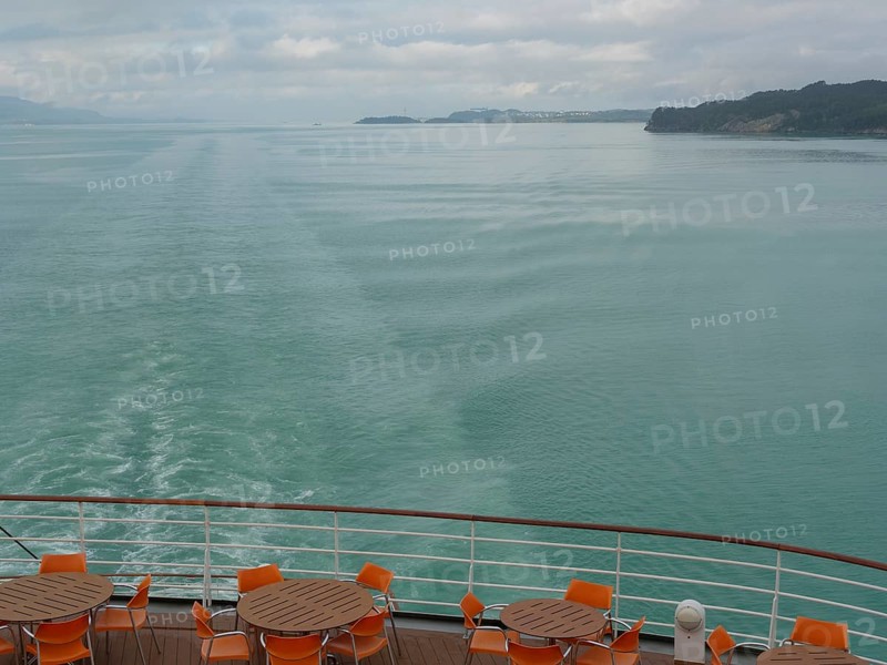Tranquil view of the sea from the back of a ship with empty table groups and orange-coloured chairs under a cloudy sky, Eidfjörd, Norway, Europe