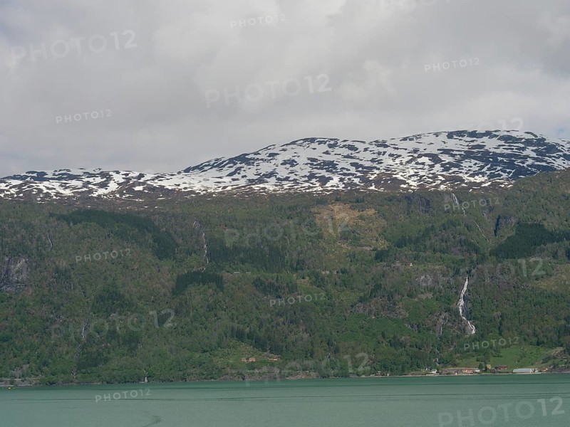 View of snow-capped mountains with waterfalls and a calm lake below, Eidfjord, Norway, Europe
