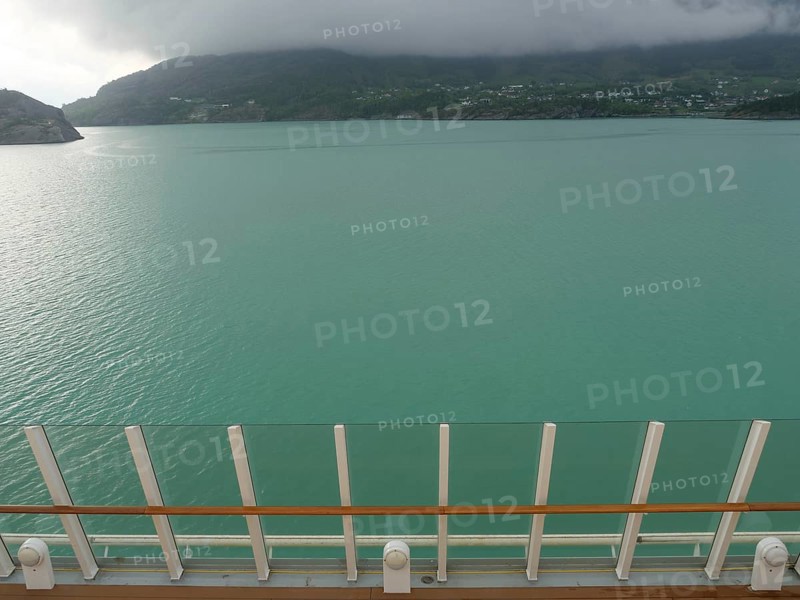 View of calm, greenish water and surrounding misty mountains, seen from a boat, eidfjord, norway
