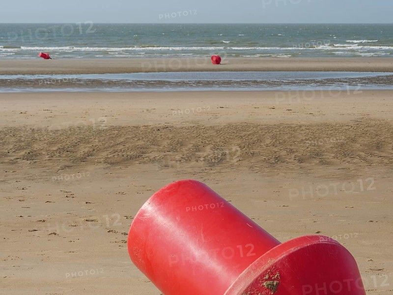 Close-up of a red buoy in the sandy beach area, with several buoys in the background and calm sea, de haan, belgium