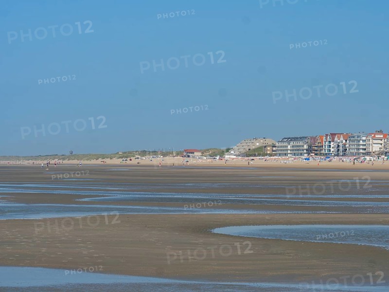 Sandy beach beach at low tide with calm sea and houses in the background under a clear blue sky, de haan, belgium