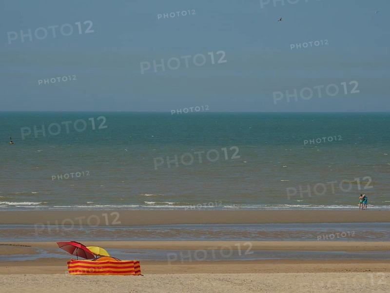 Beach with a colourful parasol and an orange and yellow striped deckchair in front of calm sea and waves, de haan, belgium