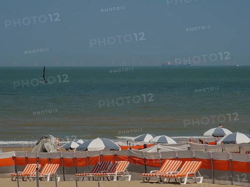 Beach full of orange and white deckchairs and parasols, a sailing boat on the sea and a blue sky, de haan, belgium