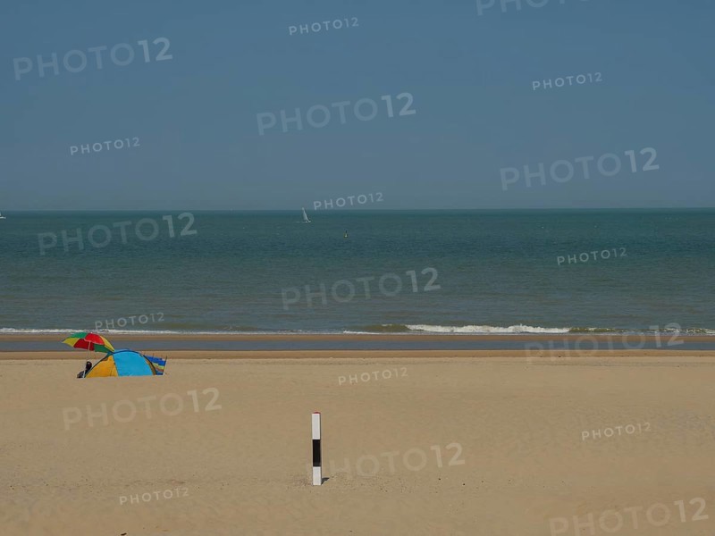 A quiet beach with a small tent in the sand, the sea in the background and a blue sky above, de haan, belgium