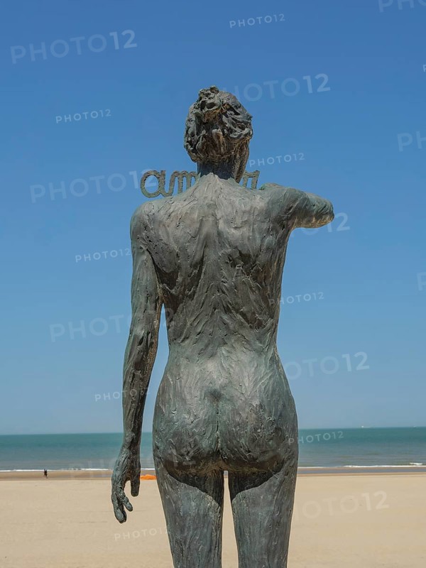 Bronze statue of a naked pregnant woman on the beach, overlooking the sea under a clear blue sky, de haan, belgium