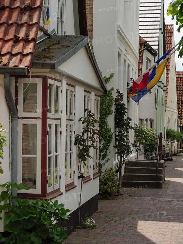 Simple residential buildings with floral decorations and a flag along a cobbled street, Kappeln, Schleswig-Holstein, Germany, Europe