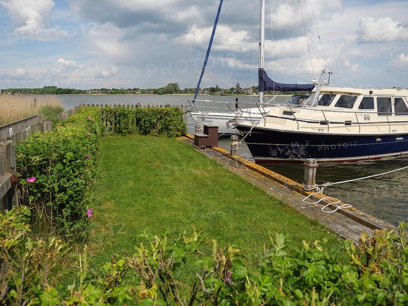 A sailing boat moored to a wooden jetty, surrounded by bushes and a cloudy sky, Arnis, Schleswig-Holstein, Germany, Europe
