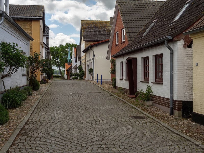 A quiet cobbled street with stylish houses and trees under a cloudy sky, Maasholm, Schleswig-Holstein, Germany, Europe