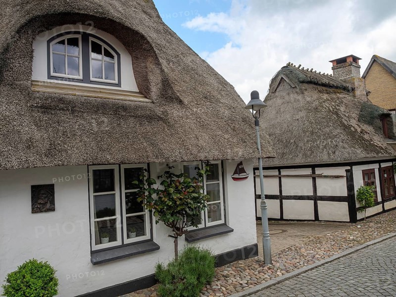 A thatched roof house on a cobbled street with windows and a street lamp under a cloudy sky, Maasholm, Schleswig-Holstein, Germany, Europe