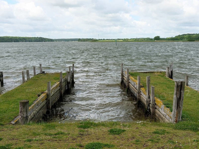 View of two harbour jetties with grass and wooden piles protruding into the water, Maasholm, Schleswig-Holstein, Germany, Europe