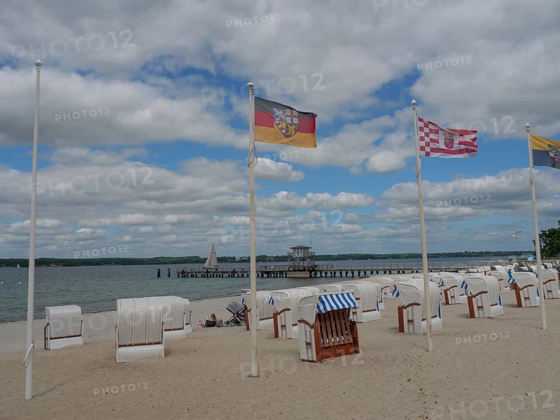 Beach chairs on a sandy beach under a cloudy sky, flags blowing in the wind, sea and jetty in the background, Glücksburg, Schleswig-Holstein, Germany, Europe
