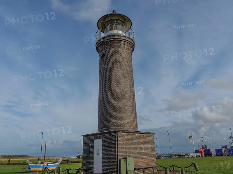 A tall brick lighthouse in a meadow with a few boats and a cloudy sky in the background, juist, east frisia, germany