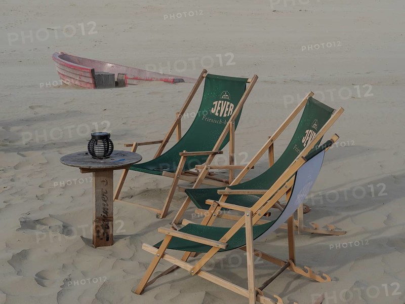 Two green deckchairs and a small table on a sandy beach, small boat in the background, Juist, East Frisia, Germany, Europe