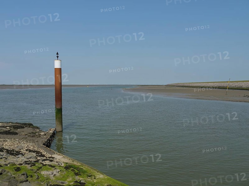 A coastal scene with a single post in calm water with clear sky and rocky shore, Hallig Hooge, schleswig-holstein, germany