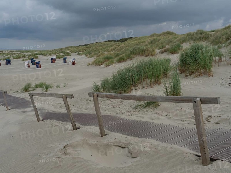 A wooden path through dunes leads to several beach chairs under a cloudy sky, juist, east frisia, germany