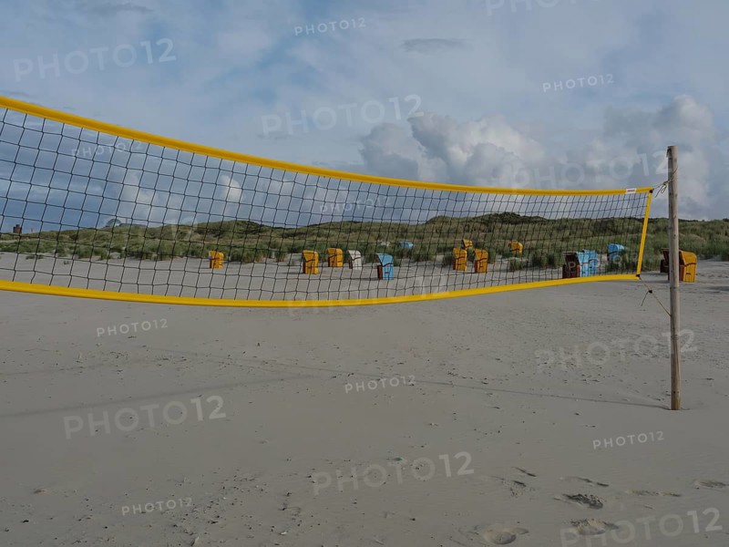 A yellow volleyball net on the beach with several beach chairs and dunes under a cloudy sky, juist, east frisia, germany