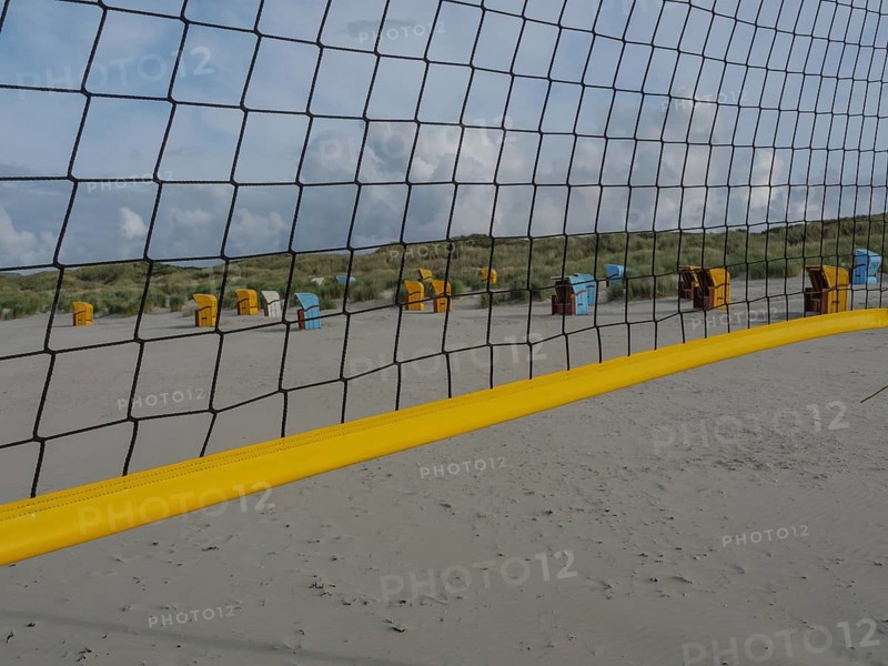 A volleyball net stretches across the beach, with dunes and beach chairs in the background, juist, east frisia, germany