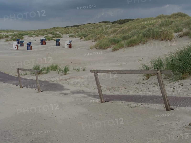Deserted beach with a wooden path and scattered beach chairs under a cloudy sky, juist, east frisia, germany