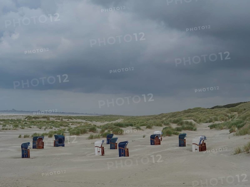 Several beach chairs scattered on the beach with dunes in the background under a grey sky, juist, east frisia, germany