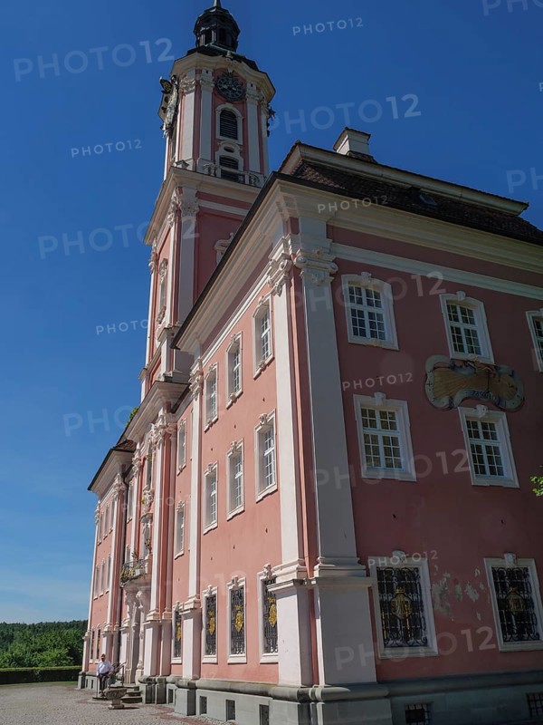 Large pink church façade with high windows under a blue sky in sunny weather, Meersburg, Germany, Europe