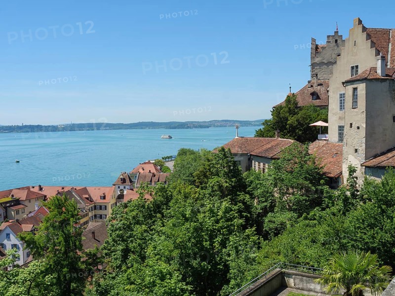 A castle and surrounding buildings on the lakeshore with lush greenery and red roofs, Meersburg, Germany, Europe