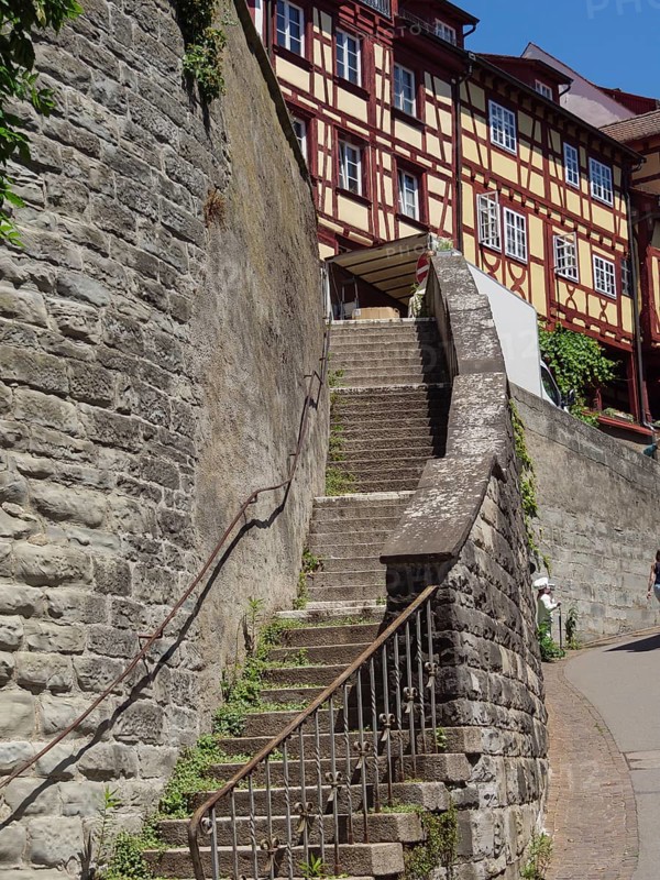 Stone staircase leads between old half-timbered houses and a stone wall in the sun, Meersburg, Germany, Europe