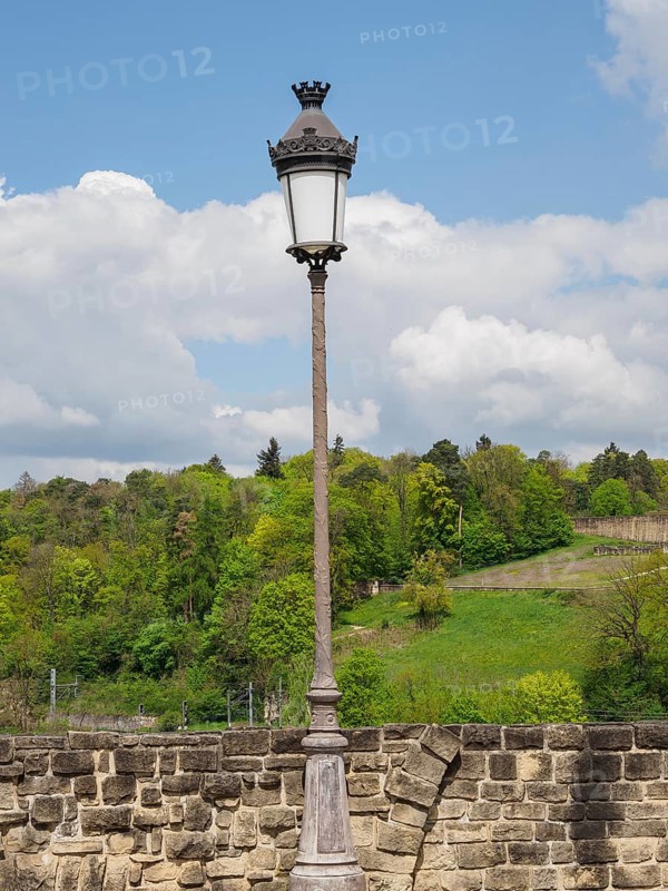 Lonely historic street lamp in front of a stone wall and a green landscape with trees and blue sky in the background, Luxembourg City, Luxembourg, Europe