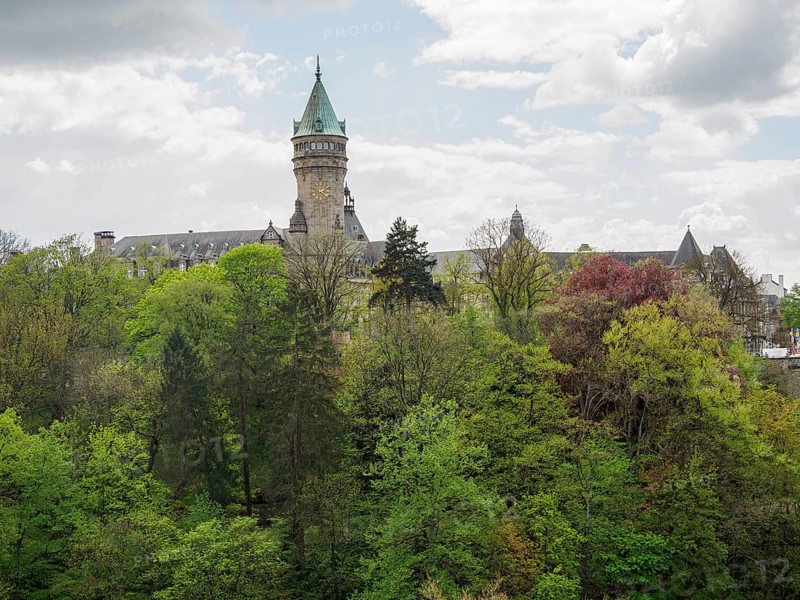 A castle with a tower stands surrounded by dense trees under a cloudy sky, Luxembourg City, Luxembourg, Europe