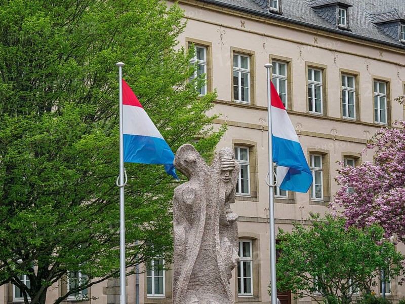 Monument with two Luxembourg flags in front of a historic building with blossoming trees, Luxembourg City, Luxembourg, Europe