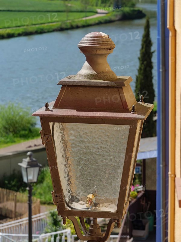 Close-up of an old street lamp next to a river, surrounded by nature, Saarburg, germany