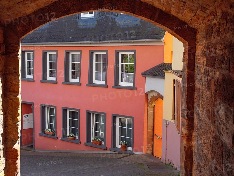 View through an archway of colourful houses in an old town with flower pots on the windowsills and a cobbled street, Saarburg, Germany, Europe