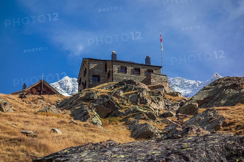 A mountain hut stands on a rocky slope with a distant snow-capped mountain range in the background, Saas Fee, Switzerland, Europe