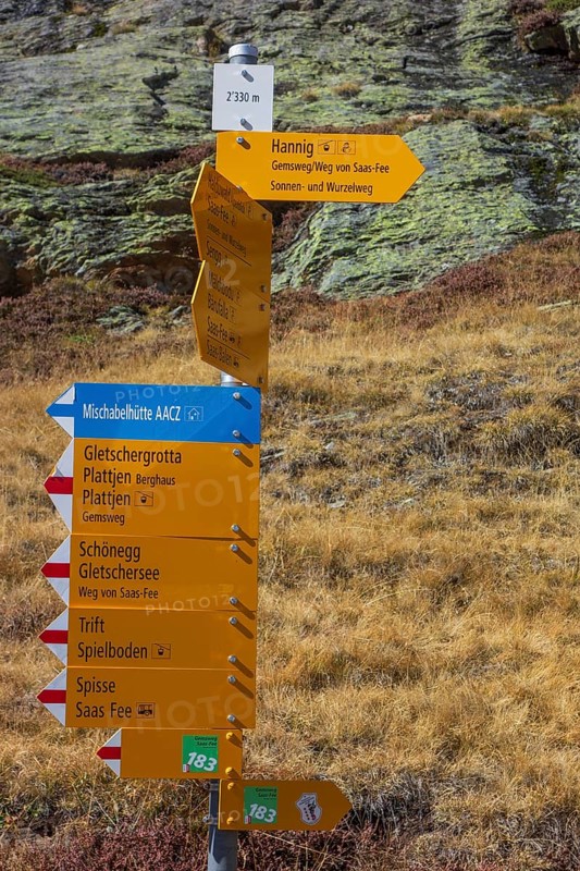 Multi-coloured hiking signposts in an autumnal Alpine landscape with information on various hiking trails, Saas Fee, Switzerland, Europe